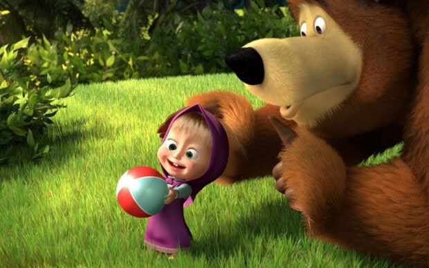 A happy girl from Masha and the Bear holding a colorful ball in the grass