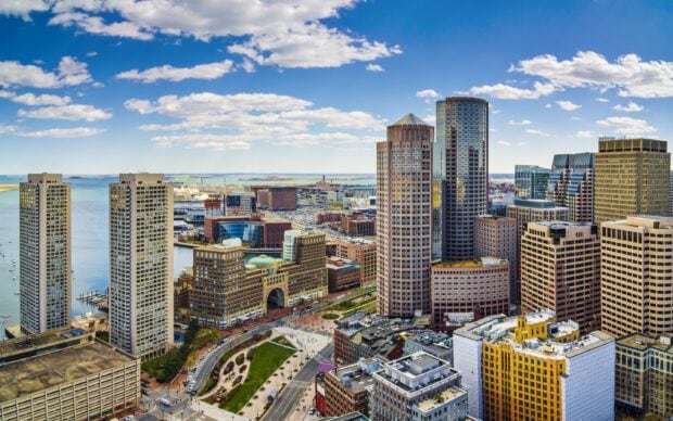 Aerial view of Massachusetts cityscape with high rise buildings and harbor under a blue sky with clouds