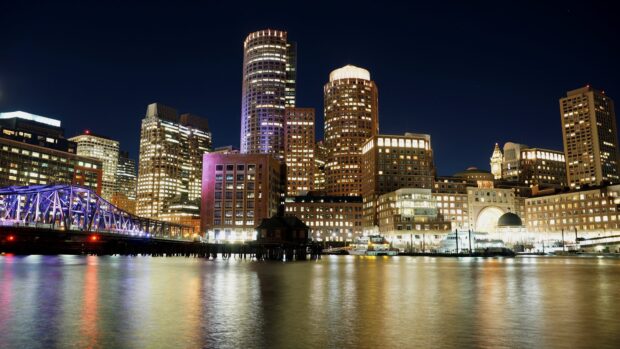 Night cityscape featuring Massachusetts skyline with illuminated buildings and bridge reflection