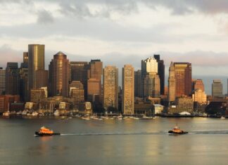 Boston city skyline featuring boats on water during sunset with Massachusetts in the background