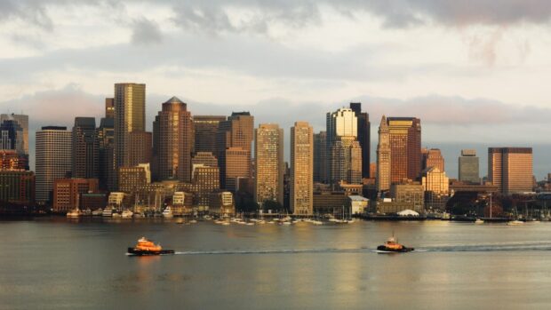 Boston city skyline featuring boats on water during sunset with Massachusetts in the background
