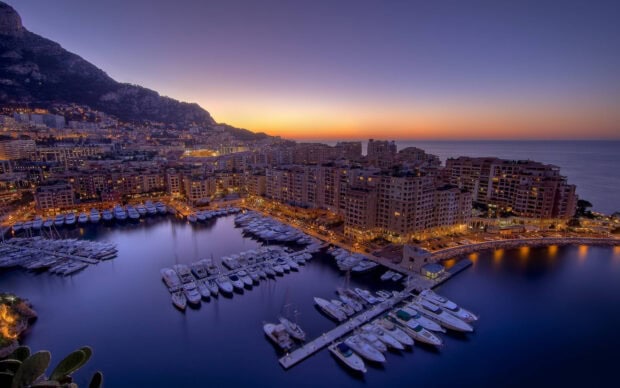 A stunning view of Monaco harbor with yachts and city lights during sunset showcasing Monaco