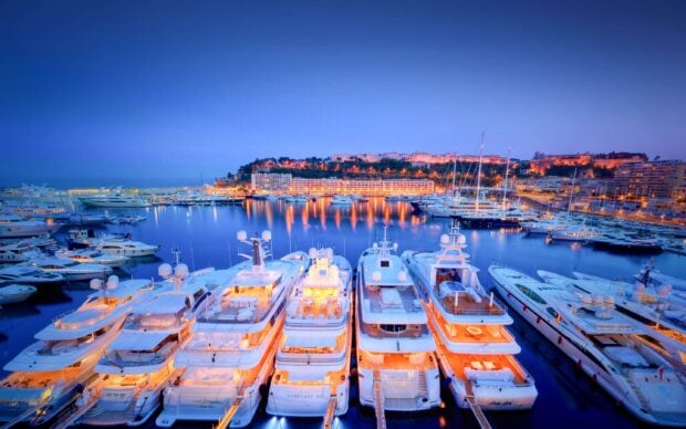 Luxury yachts docked at Monaco harbor during twilight with city lights reflecting on the water