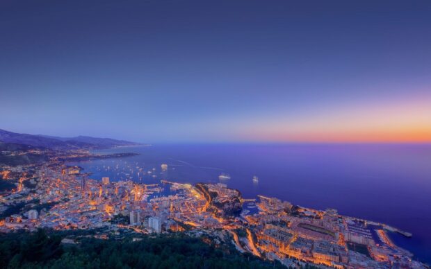 A panoramic view of Monaco cityscape during twilight with the Mediterranean Sea and yachts in the harbor