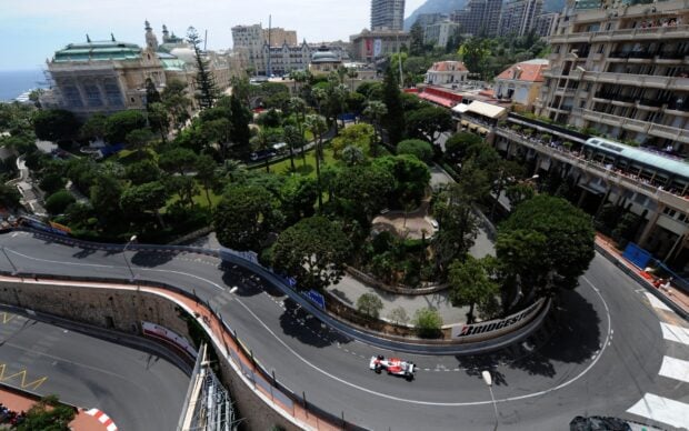 A Monaco city street circuit with a race car turning sharp corners surrounded by buildings and greenery
