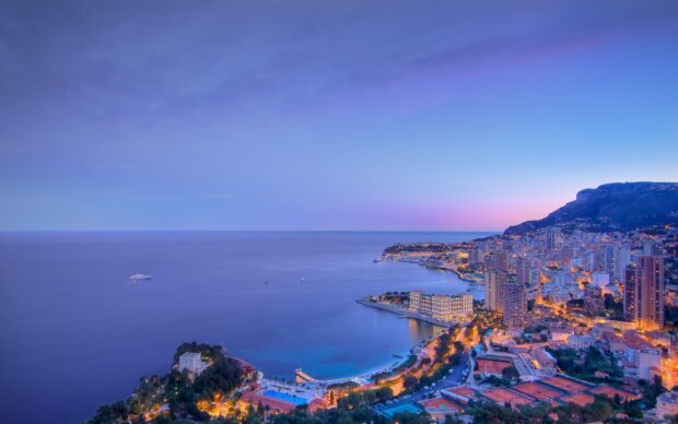 A panoramic view of Monaco coastline at dusk with city lights and the sea under a clear sky