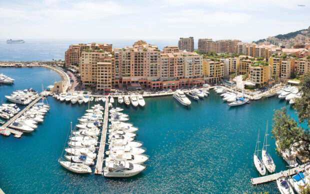 A panoramic view of Monaco with luxury yachts docked in the marina and residential buildings in the background