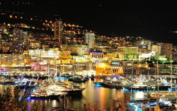 Night view of Monaco city marina with luxury yachts and illuminated buildings at night