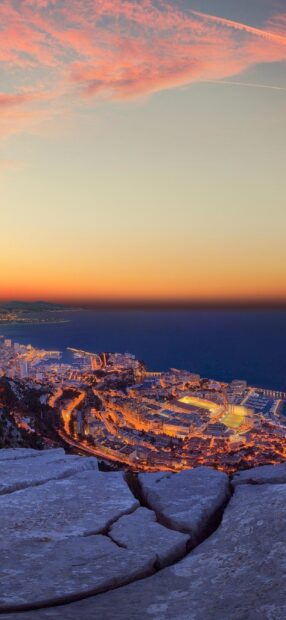 Beautiful Monaco cityscape at sunset with glowing lights and a clear sky viewed from rocky foreground