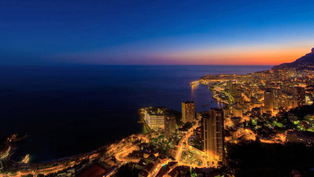 Night view of Monaco cityscape with illuminated buildings and coastline at sunset