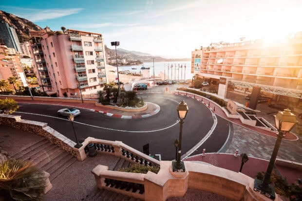 A scenic Monaco city street scene with a sharp curve and the coastal view at sunset