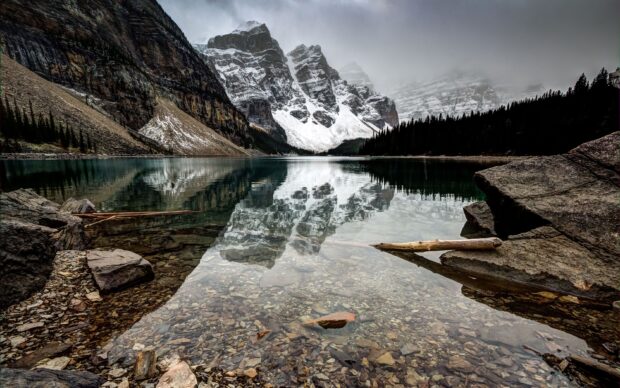 Clear water of Moraine Lake with rocky shore and snow covered mountains in the background
