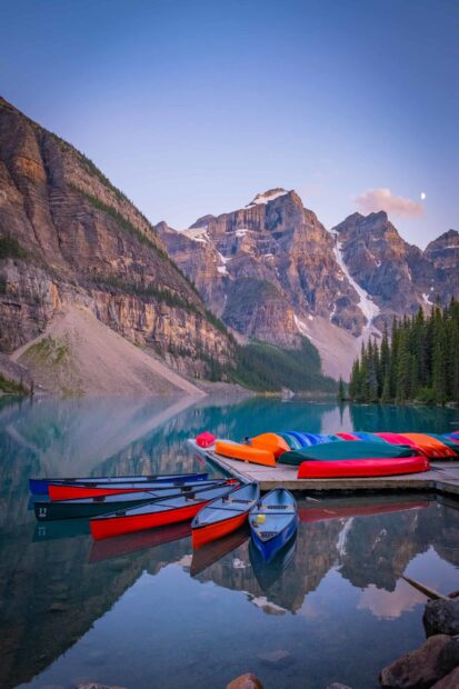 Colorful canoes lined up at Moraine Lake with towering mountains in the background
