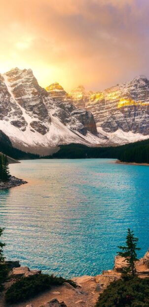 Snowy Moraine Lake surrounded by towering mountains under a golden sky