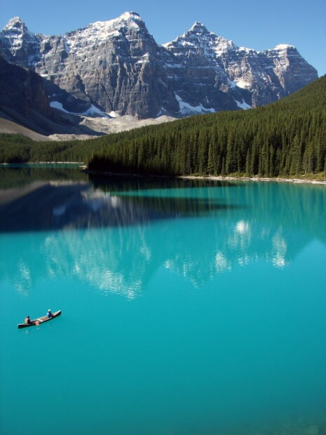 Calm turquoise water of Moraine Lake surrounded by forest and mountains with two people canoeing