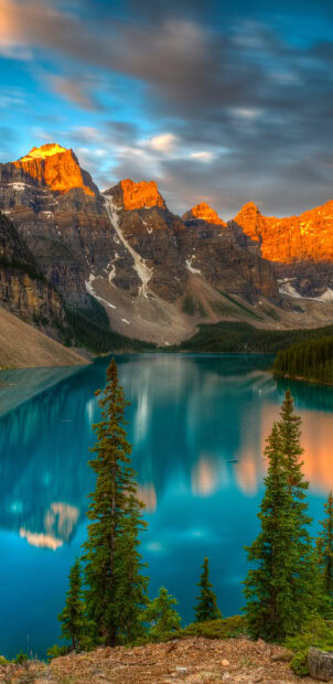 Sunrise over Moraine Lake with vibrant mountains and tall pine trees in the foreground