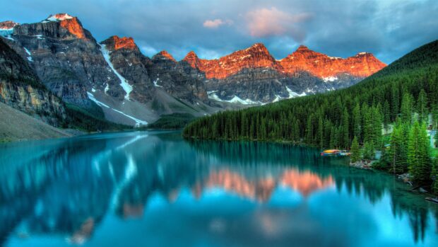 Moraine Lake surrounded by mountains and pine trees at sunset with clear blue water reflections