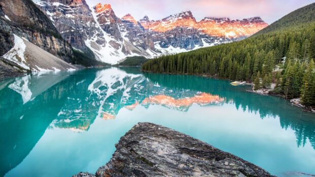 Snow capped mountains reflected in Moraine Lake with vibrant turquoise water and forest