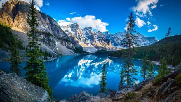 Snowy mountain peaks and pine trees around Moraine Lake reflecting in the clear blue water