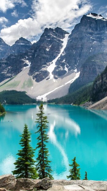 Tall green trees by Moraine Lake with turquoise water and majestic mountain peaks
