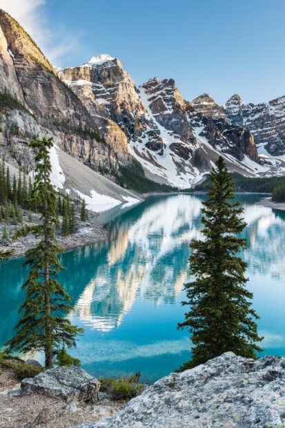 Snowy mountain peaks and green trees surrounding a clear serene lake at Moraine Lake