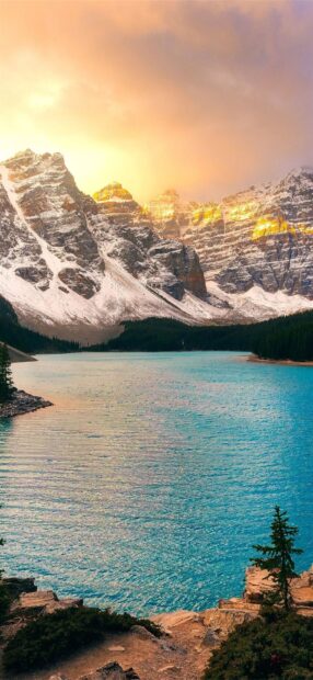 Snow capped mountains with Moraine Lake surrounded by forest at sunset