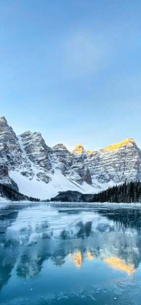Snowy Moraine Lake mountain range reflecting on the icy lake surface in the morning light