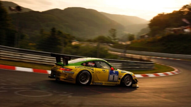 A racing car speeding on a curvy motorsports track surrounded by forested hills at sunset