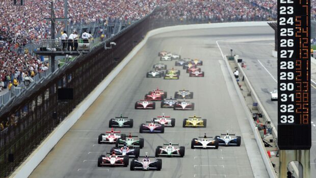 IndyCar race cars compete on a large track during a high speed motorsports event