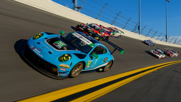 Blue Porsche race car leading a pack of GTD class motorsports cars on a banked race track