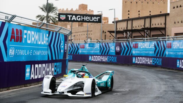 Formula E race car driving on city circuit with sponsorship banners