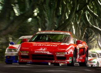 Red Honda race car leading other cars on a forest road during a motorsports race