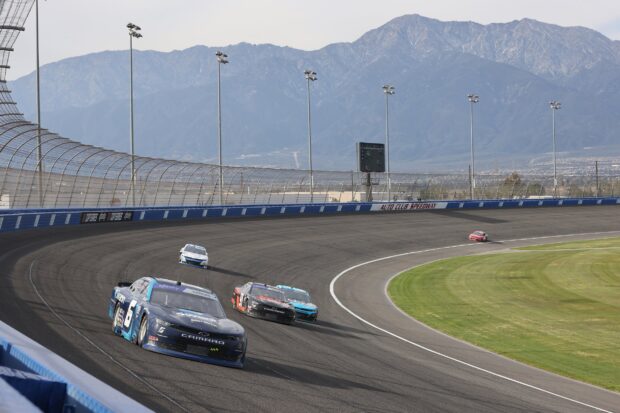 Stock cars racing on a curved speedway track with mountains in the background