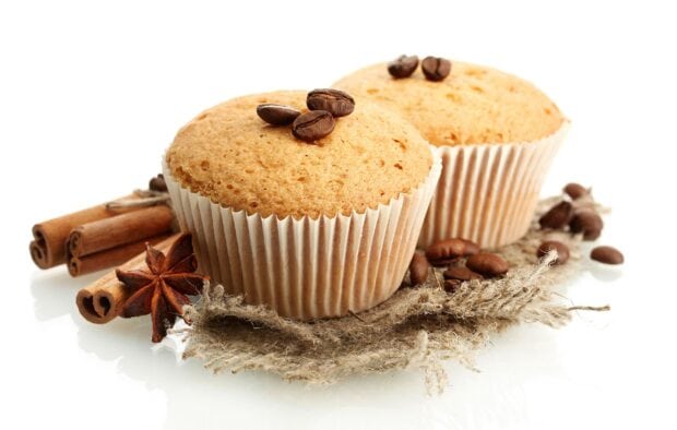 Two muffins with coffee beans and cinnamon placed on a rustic fabric