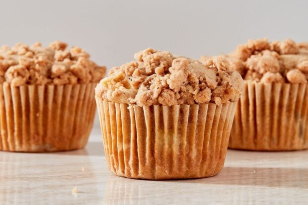 A crumbly muffin with streusel topping in focus on a marble surface