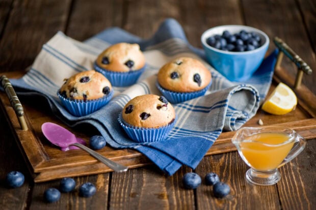 Blueberry muffins on a wooden tray with fresh blueberries and honey