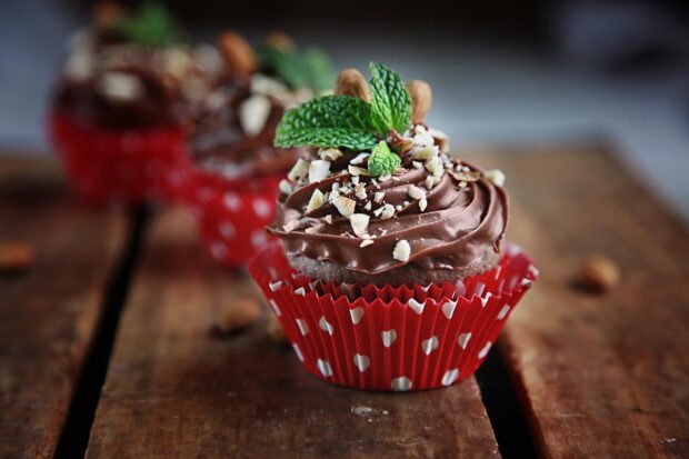 Chocolate muffin topped with mint leaves and crushed nuts in a red polka dot cup