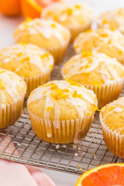A close up of a lemon muffin with icing and orange zest on a cooling rack