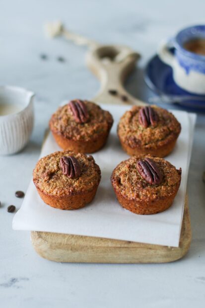A close up of freshly baked muffin topped with a pecan nut on a wooden board
