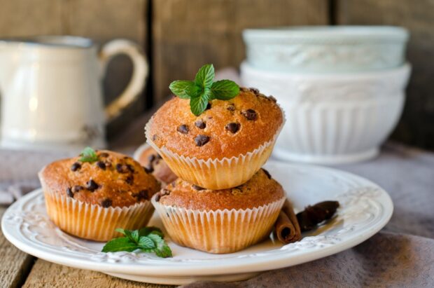 Chocolate chip muffin with fresh mint on a white plate in a rustic setting