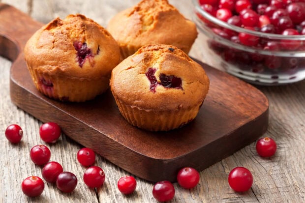 Fresh muffin with cranberry pieces on wooden board