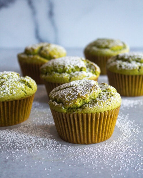 Green muffin topped with powdered sugar sitting on a table with more muffins in the background