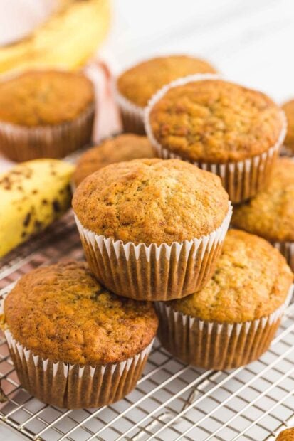 Fresh banana muffins stacked on a cooling rack with ripe bananas in the background