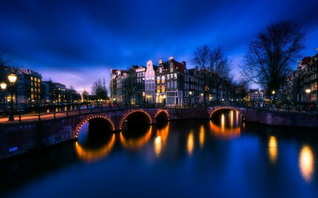 Historic canal houses along illuminated Amsterdam canal at dusk in Netherlands