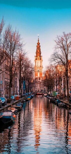 Amsterdam canal with historic tower and boats reflecting in water during sunset in Netherlands