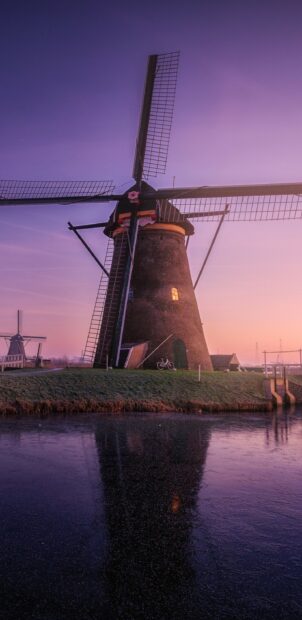 Traditional Netherlands windmill stands beside calm water at sunset