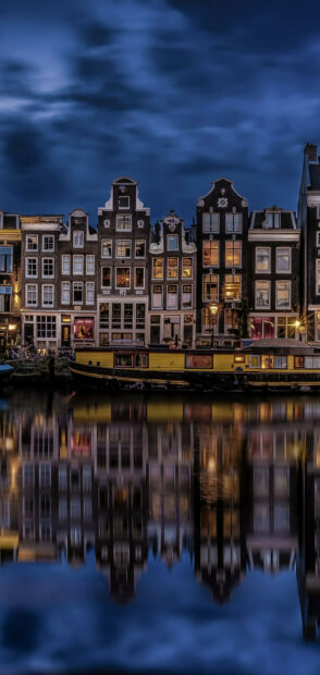 Historic canal houses in Netherlands reflecting on water at night with a moored boat
