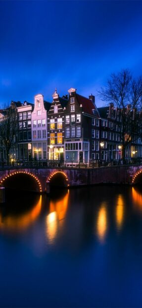 Historic Dutch buildings along the canal in the Netherlands at dusk with illuminated bridge lights