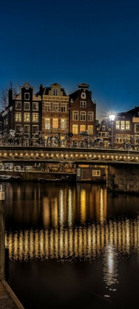 Nighttime view of Netherlands canal with historic buildings and bicycles on bridge