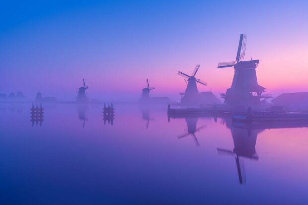 Traditional Netherlands windmills reflected on calm water during sunrise haze